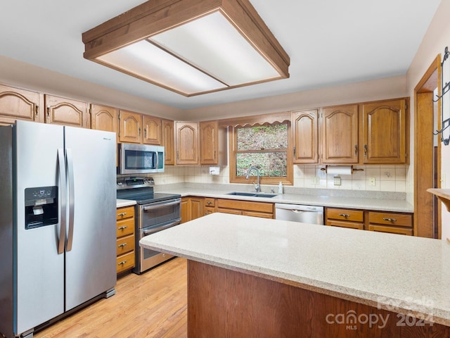 kitchen with light wood-type flooring, stainless steel appliances, backsplash, and sink