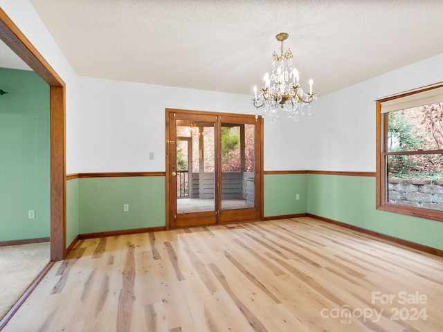 empty room featuring a chandelier, light hardwood / wood-style flooring, a healthy amount of sunlight, and a textured ceiling