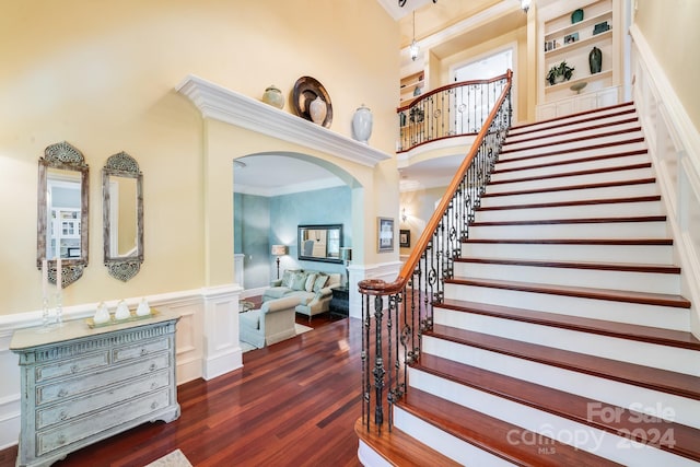 entryway featuring arched walkways, dark wood finished floors, wainscoting, stairway, and a high ceiling