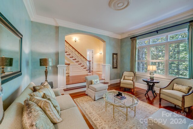 living room featuring stairs, arched walkways, wood finished floors, and crown molding