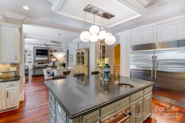 kitchen featuring arched walkways, open floor plan, stainless steel built in fridge, a kitchen island with sink, and a sink