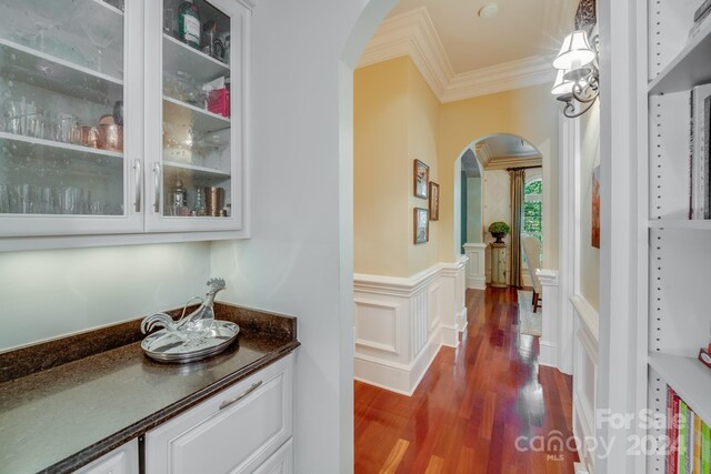 hallway with arched walkways, a wainscoted wall, dark wood finished floors, crown molding, and a decorative wall