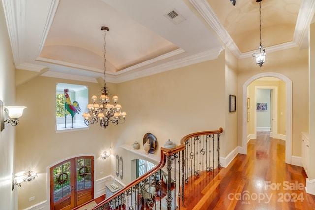 corridor with arched walkways, french doors, a raised ceiling, and wood finished floors