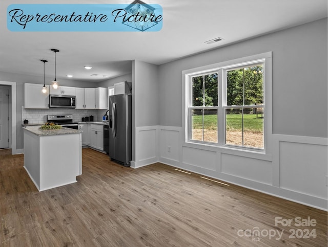 kitchen featuring appliances with stainless steel finishes, decorative light fixtures, white cabinetry, tasteful backsplash, and light hardwood / wood-style floors