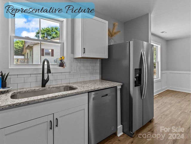 kitchen with white cabinetry, stainless steel appliances, tasteful backsplash, light stone counters, and sink