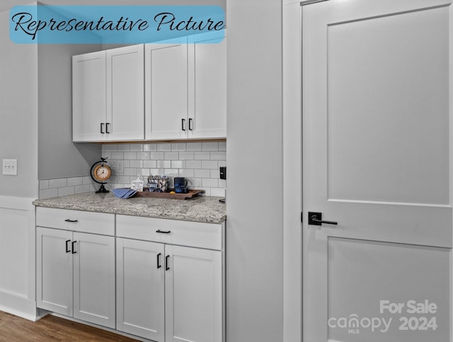 interior space featuring decorative backsplash, light stone countertops, hardwood / wood-style floors, and white cabinets