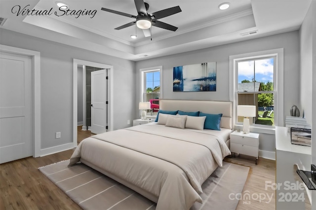 bedroom with ceiling fan, wood-type flooring, a tray ceiling, and ornamental molding