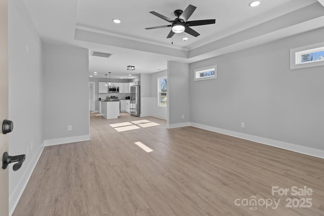 unfurnished living room with plenty of natural light, a raised ceiling, and light hardwood / wood-style floors