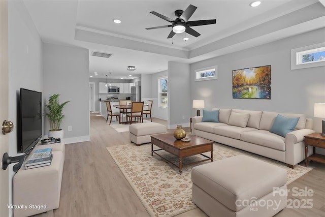 living room featuring plenty of natural light, a tray ceiling, and light hardwood / wood-style floors