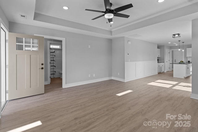 unfurnished living room with crown molding, ceiling fan, light hardwood / wood-style floors, and a tray ceiling