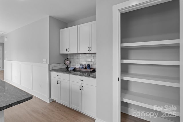 bar featuring backsplash, white cabinets, light hardwood / wood-style floors, and dark stone counters