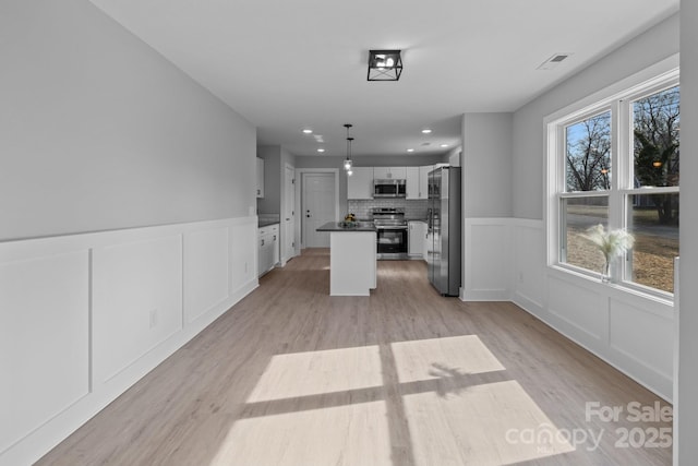 kitchen with white cabinetry, stainless steel appliances, a kitchen island, decorative light fixtures, and light wood-type flooring