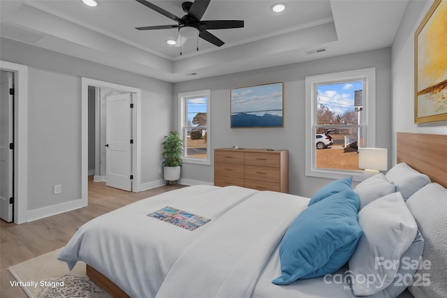 bedroom with multiple windows, light hardwood / wood-style floors, a raised ceiling, and ceiling fan