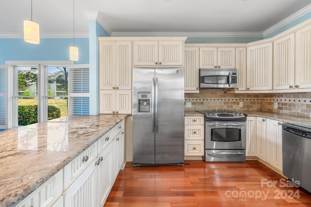 kitchen featuring cream cabinets, crown molding, appliances with stainless steel finishes, light hardwood / wood-style floors, and pendant lighting