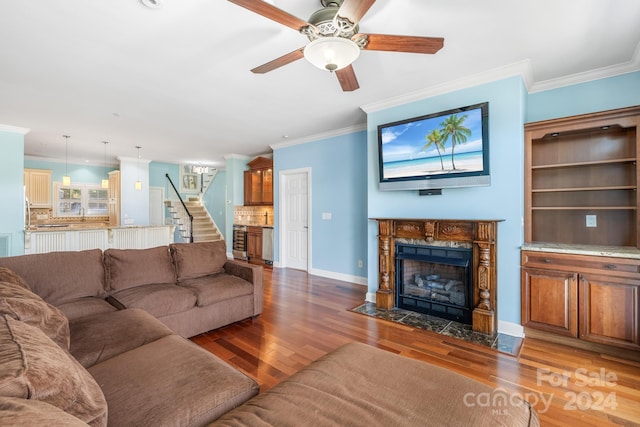 living room with crown molding, ceiling fan, a tiled fireplace, and hardwood / wood-style flooring