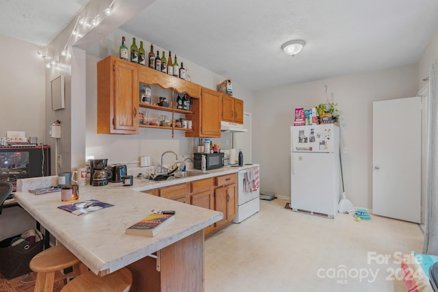 kitchen featuring a kitchen breakfast bar, sink, kitchen peninsula, and white appliances