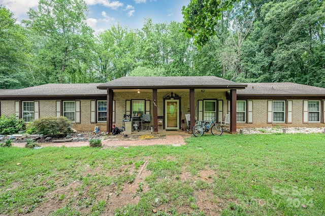 ranch-style home featuring brick siding, covered porch, a front yard, and a shingled roof