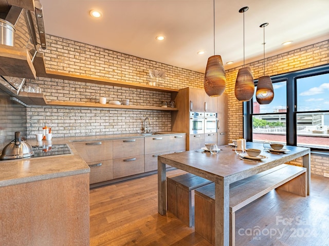 kitchen featuring decorative light fixtures, light hardwood / wood-style floors, gas cooktop, sink, and brick wall