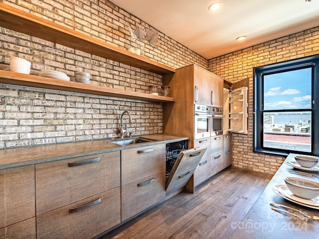 kitchen with oven, brick wall, dark hardwood / wood-style floors, and sink