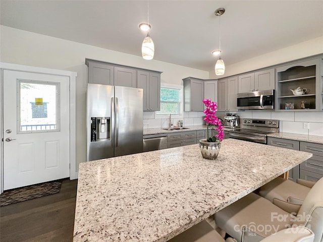 kitchen featuring tasteful backsplash, sink, hanging light fixtures, light stone countertops, and stainless steel appliances