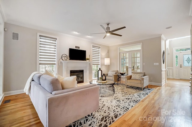 living room with crown molding, a wealth of natural light, light wood-type flooring, and french doors