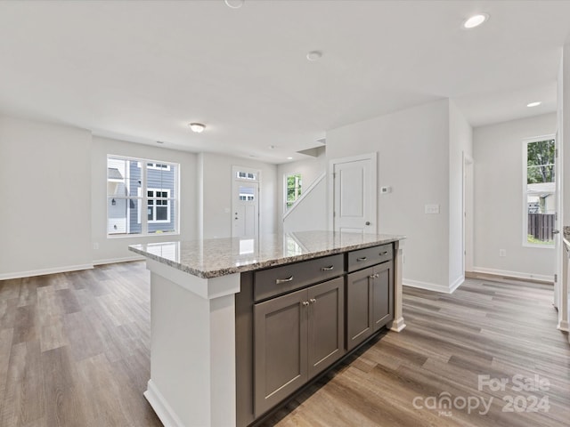 kitchen with wood-type flooring, light stone countertops, and a kitchen island