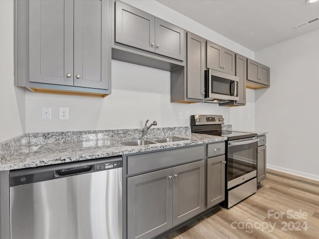 kitchen with gray cabinetry, light wood-type flooring, stainless steel appliances, light stone countertops, and sink