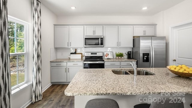 kitchen with appliances with stainless steel finishes, sink, backsplash, light stone counters, and a breakfast bar