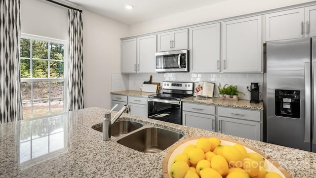 kitchen with light stone countertops, appliances with stainless steel finishes, decorative backsplash, and sink