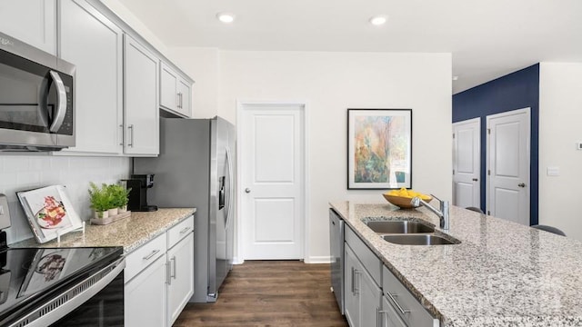 kitchen with backsplash, dark hardwood / wood-style floors, sink, appliances with stainless steel finishes, and light stone counters