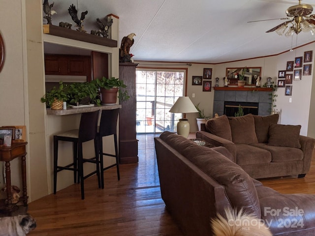 living room featuring a tiled fireplace, dark wood-type flooring, a textured ceiling, and ceiling fan