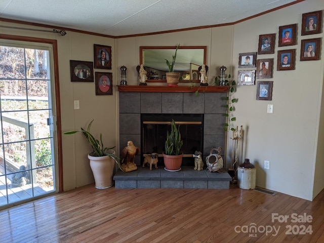 living room featuring hardwood / wood-style floors, ornamental molding, a textured ceiling, and a tiled fireplace