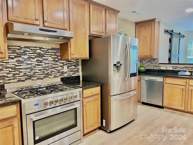 kitchen with appliances with stainless steel finishes, dark stone counters, light hardwood / wood-style flooring, and backsplash