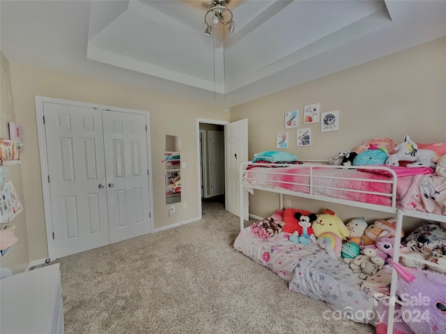 bedroom featuring ceiling fan, a closet, light colored carpet, and a tray ceiling