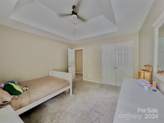 bedroom with ceiling fan, a raised ceiling, carpet flooring, and a closet