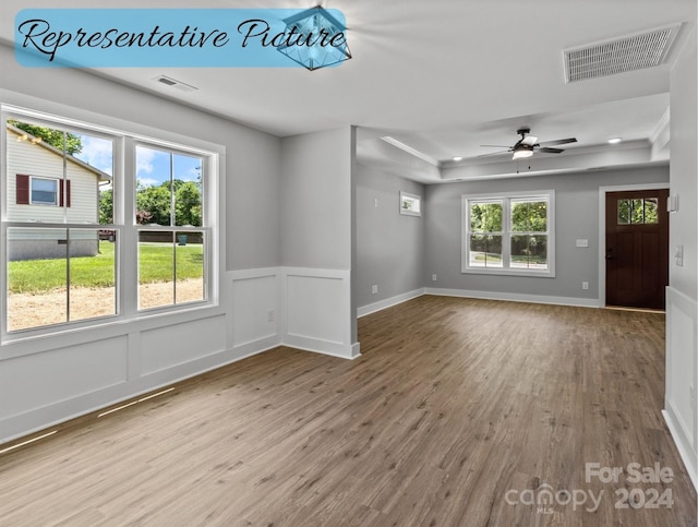 unfurnished living room with ceiling fan, hardwood / wood-style floors, and a tray ceiling