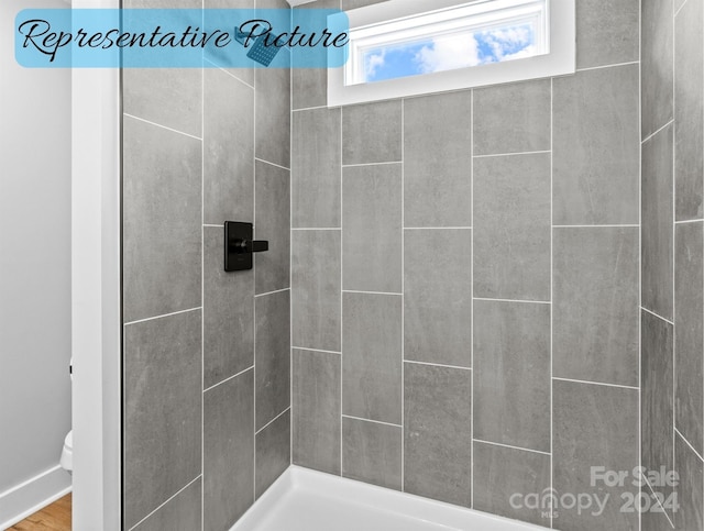 bathroom with tiled shower, toilet, and hardwood / wood-style floors