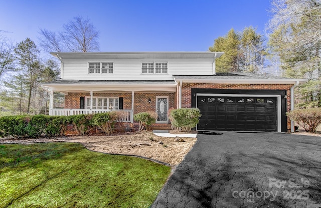 traditional-style home with a porch, aphalt driveway, a garage, brick siding, and a front yard