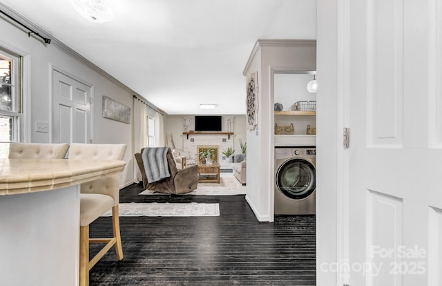 interior space with a fireplace with raised hearth, washer / clothes dryer, dark wood-type flooring, and ornamental molding