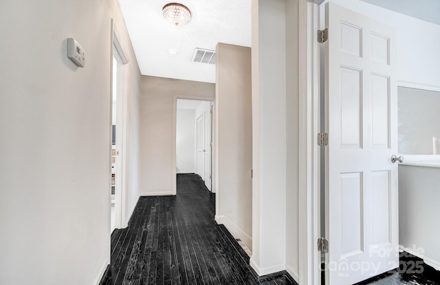 hall featuring dark wood-style flooring, visible vents, and baseboards