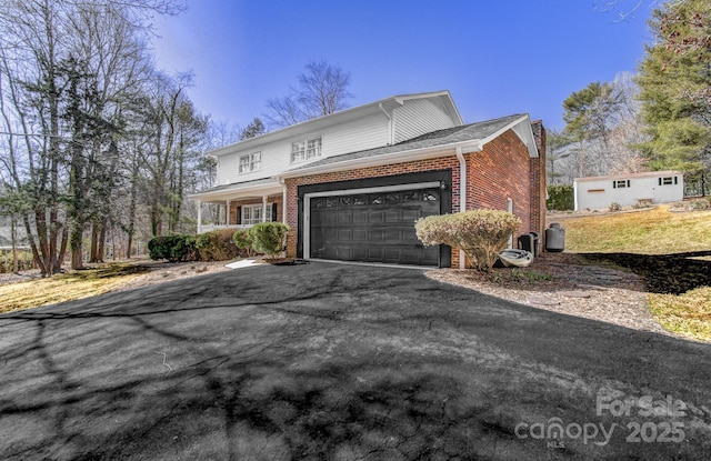 traditional-style home featuring an attached garage, brick siding, a porch, and aphalt driveway