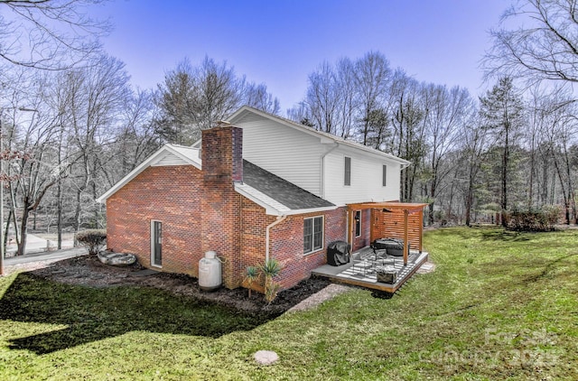 view of side of home with roof with shingles, brick siding, a lawn, and a chimney