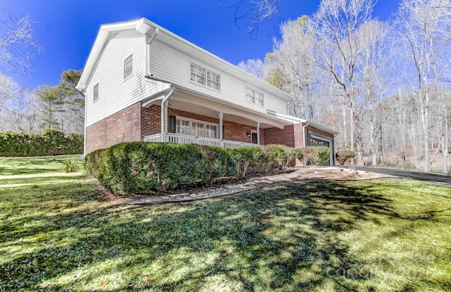 view of side of property with a garage, brick siding, a lawn, and a porch