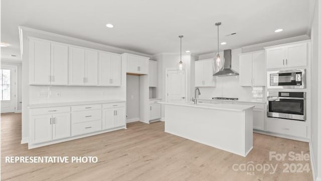 kitchen featuring wall chimney range hood, white cabinetry, stainless steel oven, a kitchen island with sink, and built in microwave