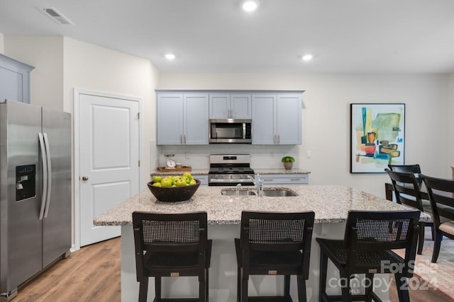 kitchen featuring sink, appliances with stainless steel finishes, an island with sink, gray cabinetry, and light stone counters