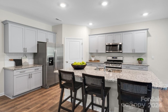 kitchen with a kitchen island with sink, gray cabinets, stainless steel appliances, and a kitchen bar