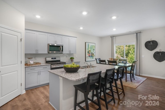 kitchen featuring decorative backsplash, a kitchen island with sink, light stone countertops, a breakfast bar area, and stainless steel appliances