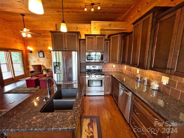 kitchen featuring pendant lighting, sink, dark stone countertops, stainless steel appliances, and dark hardwood / wood-style flooring