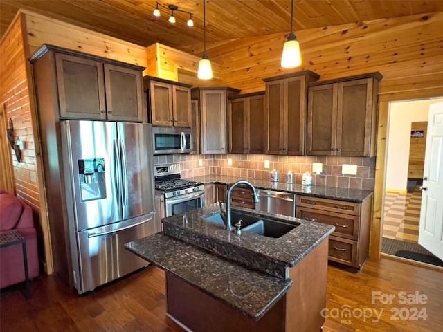 kitchen with hanging light fixtures, stainless steel appliances, an island with sink, wooden ceiling, and dark stone counters