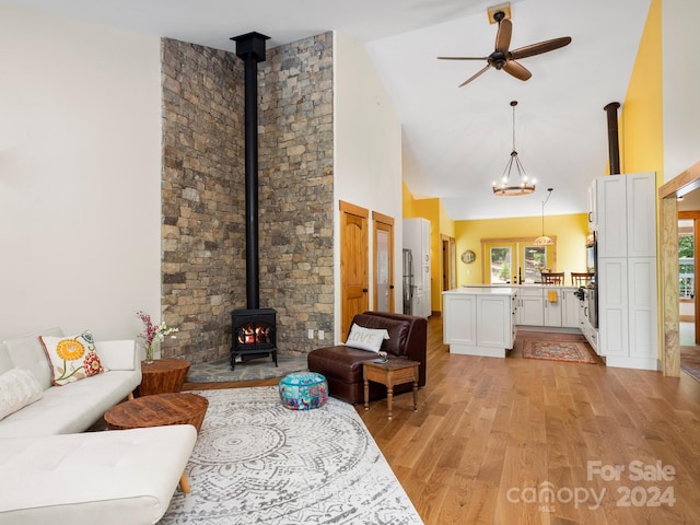 living room featuring high vaulted ceiling, a wood stove, ceiling fan, and light wood-type flooring